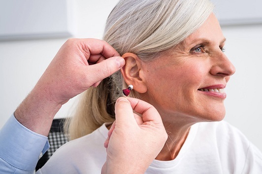 Seniorin bekommt modernes Hörgerät eingesetzt, Hörakustiker passt Hörsystem an.